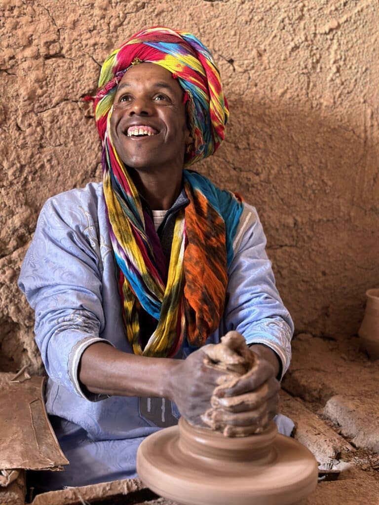 Artisan potier marocain souriant en façonnant de l'argile dans un atelier traditionnel.