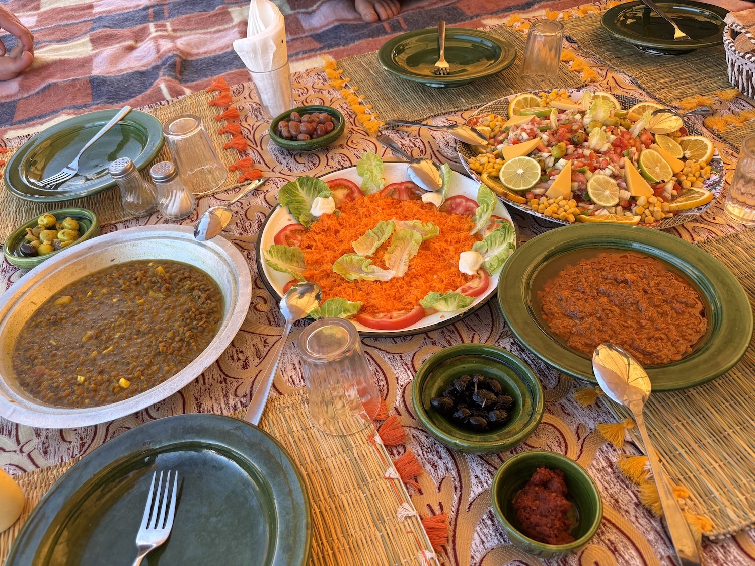 Repas convivial partagé dans le désert marocain pendant le séjour du Nouvel An, avec des plats traditionnels et une ambiance chaleureuse.