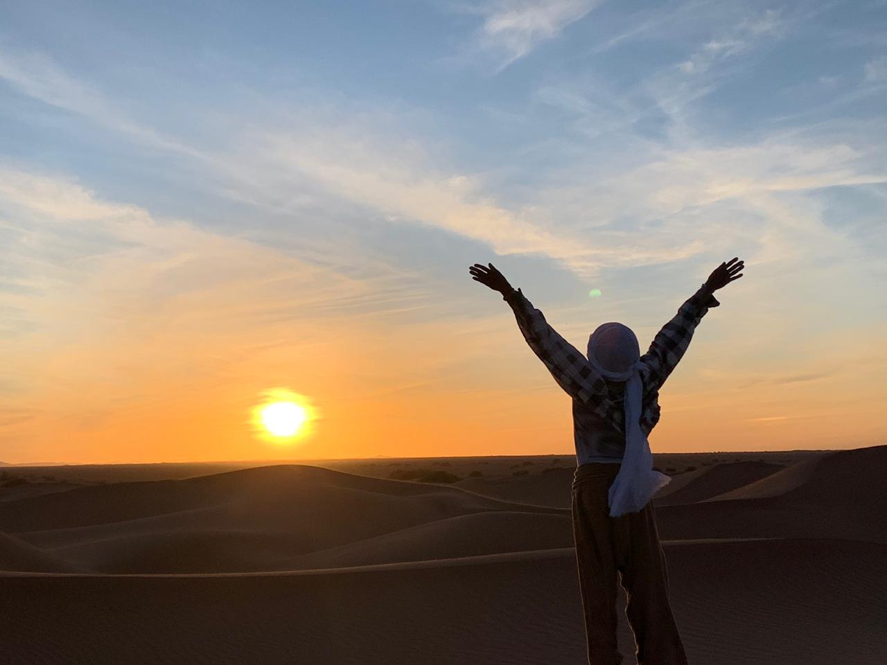 Personne levant les bras au lever du soleil dans le désert marocain pendant une retraite spirituelle