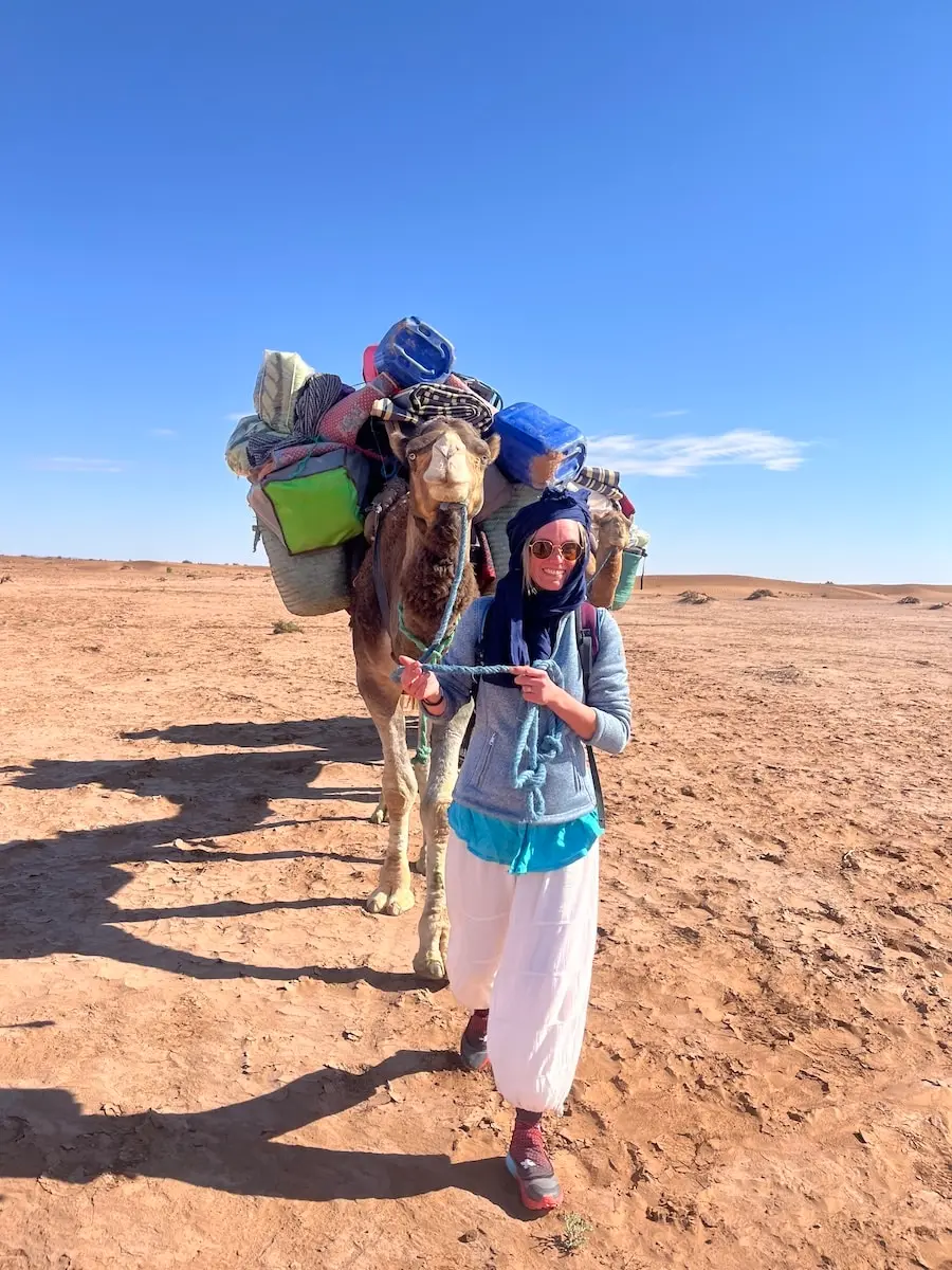 Vie nomade dans le désert – Retraite spirituelle au Maroc Participant guidant un dromadaire dans le désert lors d’une retraite spirituelle au Maroc
